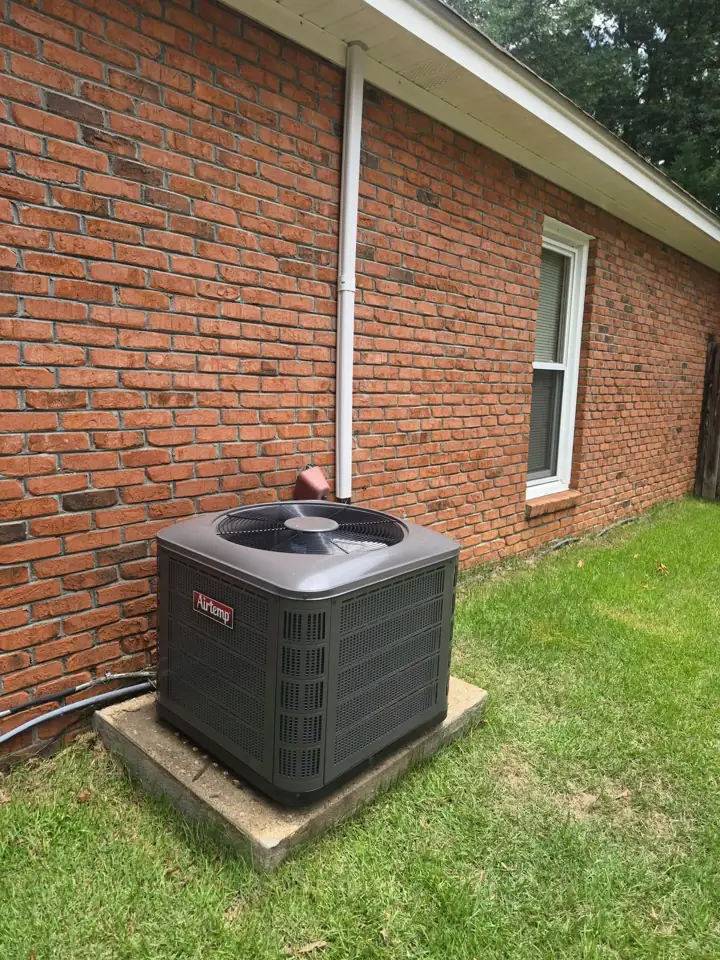 New Airtemp central air conditioner installed on a concrete pad beside a red brick home