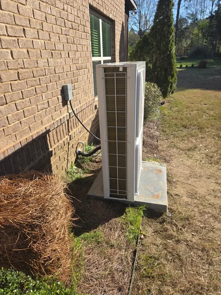 Newly installed outdoor heat pump unit on a concrete pad beside a brick home